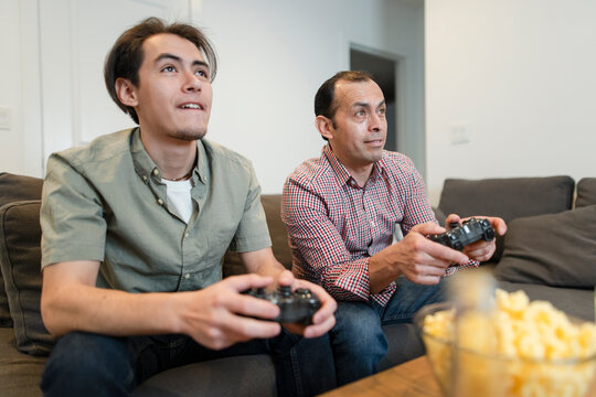 Father and son playing video game together on living room sofa