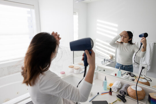 Young woman getting ready, drying hair in morning bathroom