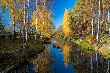 Stunning autumn scenery with river, yellowed birch trees and vintage boat reflected in still water