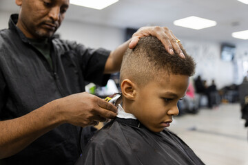Barber with electric razor giving boy fade haircut in barber shop