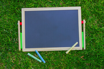close up small empty black chalkboard and colors chalks on green grass, , top view