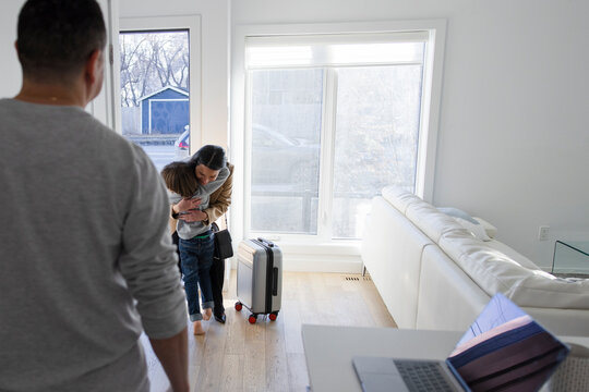 Son hugging, greeting mother returning home from business trip