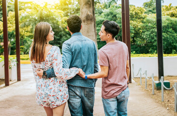 Unfaithful girl walking in the park with her boyfriend while holding another man hand. Love...