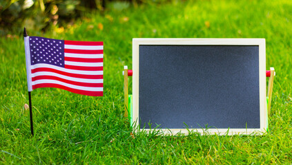 close up black blank chalk board and flag of USA on green lawn. place for text, copy space.
