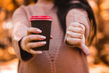 Pregnant woman standing in autumn city park forest, showing dislike thumb down sign gesture, refuses drinking hot beverage coffee tea, prohibition, ban. Fall time. Mother's love, pregnancy concept
