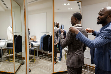 Tailor measuring customer for suit at mirror in menswear shop