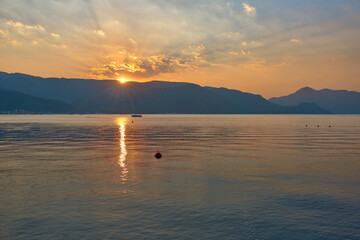 View of the rising sun over the mountains in the bay of Marmaris. Reflections of the sun in the water. The rays come out of the disk of the sun.