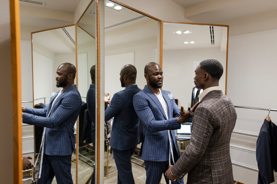Tailor fitting customer for suit at mirror in menswear shop
