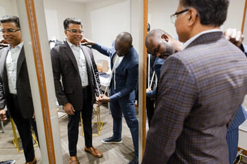 Male tailor measuring customer for suit at mirror in menswear shop