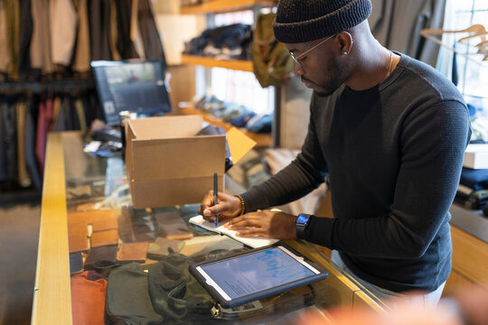 Male business owner writing in notebook at clothing store counter