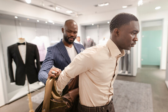 Tailor helping customer trying on suit in menswear shop