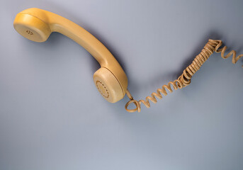 Yellow telephone receiver with twisted cord from an old antique rotary phone on blue background. Plastic removed handset from retro phone with cable. Concept of communication. Top view. - obrazy, fototapety, plakaty