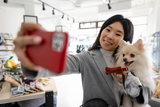 Woman with cute dog and bowtie taking selfie in pet store