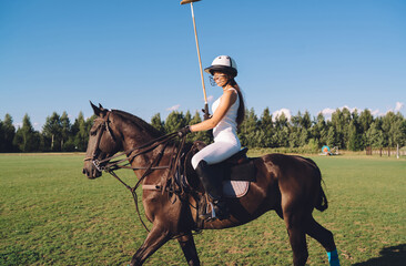 Delighted female equestrian riding horse with mallet in hand on polo field