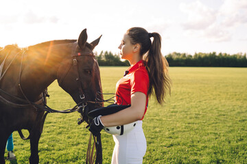 Female equestrian caressing horse on green field