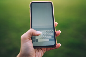 Anonymous person messaging on mobile phone against verdant grass