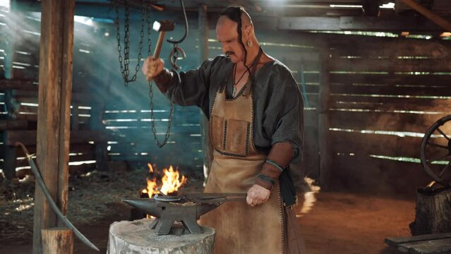 Blacksmith in the forge forges a horseshoe. Blacksmith makes iron products. Flames of fire in the Forge workshop. Zaporozhian Cossack.