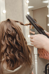 Naklejka premium girl in beauty salon is doing her hair. women's hair styling on flat iron. blog aesthetics, beauty, hair stylists. hair curling curling iron, space for text.