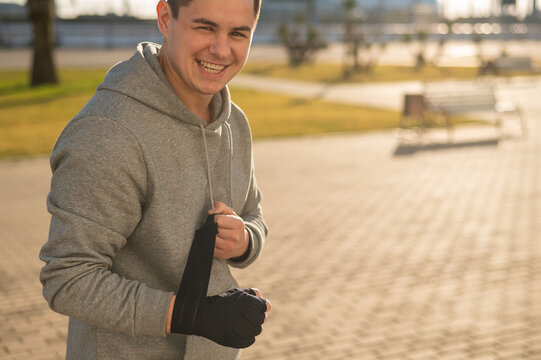 Caucasian Man In Hoodie Bandaging His Hands Before Boxing Class Outdoors.