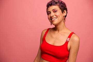 Fashion portrait of a woman with a short haircut of purple color and a smile with teeth in a red top on a pink background happiness