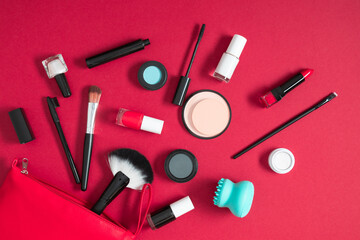 Flat lay, top view of red cosmetics bag with makeup products scattered on red background with space. Beauty background with facial cosmetic products.