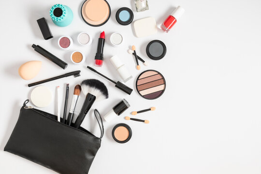 Flat lay, top view of black cosmetics bag with makeup products scattered on white background with space. Beauty background with facial cosmetic products.