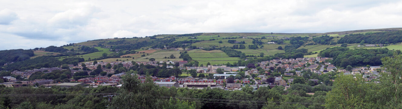 a long panoramic view of the town of mytholmroyd from above with buildings and streets of the town visible in the valley with surrounding pennine hills and fields