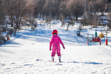 Child athlete skier standing on the ski slope of a snowy mountain preparing for a downhill skiing...
