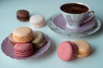 Mix of appetizing macarons and delicious coffee in porcelain cup on white table decorated with blurred flowers. Dry flowers. Greeting card.