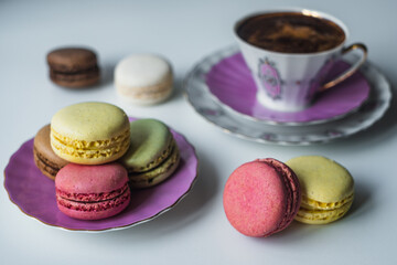 Mix of appetizing macarons and delicious coffee in porcelain cup on white table decorated with blurred flowers. Dry flowers. Greeting card.