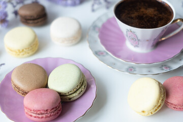 Mix of appetizing macarons and delicious coffee in porcelain cup on white table decorated with blurred flowers. Dry flowers. Greeting card.
