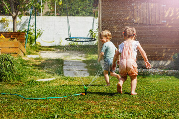 Two kids have fun in the garden - playing with water on lawn
