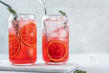 Blood Orange lemonade cocktail with ice and thyme on light gray concrete background