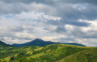 Beautiful summer landscape with forested hills, mount Strymba in the distance, and sky with low clouds. Carpathian mountains, Ukraine