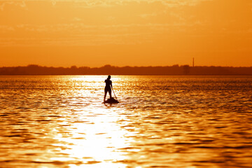 Fototapeta na wymiar silhouette of a teenage girl on a Stand Up Paddle Board SUP. Golden sunset sky reflecting in the water. Greifswalder Bodden, Baltic Sea 