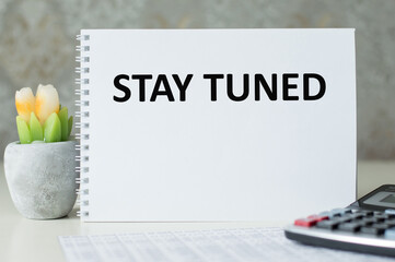 On a light background, a white notebook with the words STAY TUNED - Powered by Adobe