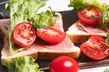 Close-up of delicious toasts decorated with microgreens and tomatoes and fresh lettuce. Healthy breakfast. Green towel in background. White background.	