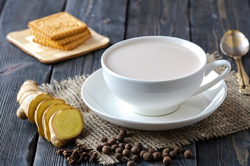 Traditional Indian drink masala chai with spices of ginger, black pepper, cloves, biscuits and a spoon on a wooden background