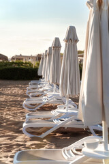 Rows of folded beach parasols and empty loungers on the background of sand. Resort hotel. End of tourist season concept.