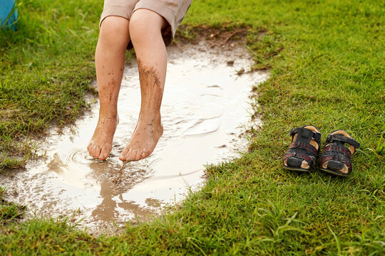 Ni&ntilde;o feliz jugando a columpiarse en el parque al aire libre mojando sus pies en el lodo en un charco de agua por la lluvia