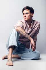 Male portrait on a gray background. A young guy in blue jeans and a shirt on a gray background. Model looking guy