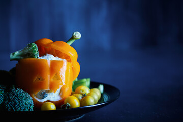 Colorful stuffed sweet orange bell pepper as monster with cut out face carved into a Halloween...