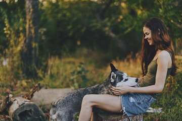 A woman laughs while playing with her husky dog ​​in a park among the trees in the forest and laughs happily. Lifestyle truthful friends people with animals