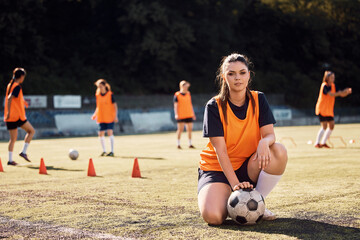 Female soccer player with ball during sports training on stadium looking at camera.