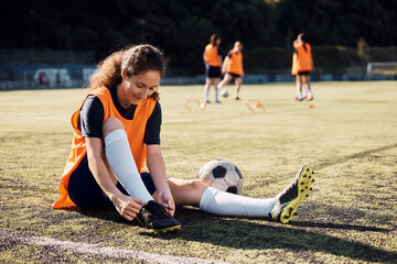 Female player tying shoelace during soccer training on stadium.