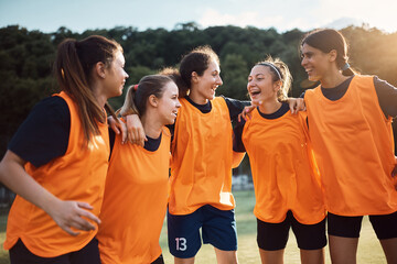 Cheerful female soccer team huddling while celebrating on playing field.