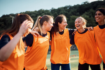 Happy female soccer players embrace while celebrating victory on playing field.