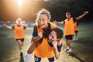 Happy female players celebrating a goal during soccer match at stadium.