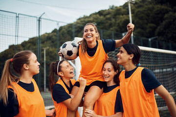 Happy women's soccer team carrying one of players while celebrating wining the match on playing field. - Powered by Adobe