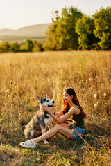 Naklejka na ściany i meble Woman sitting in field with dachshund dog smiling while spending time in nature with friend dog in autumn at sunset while traveling